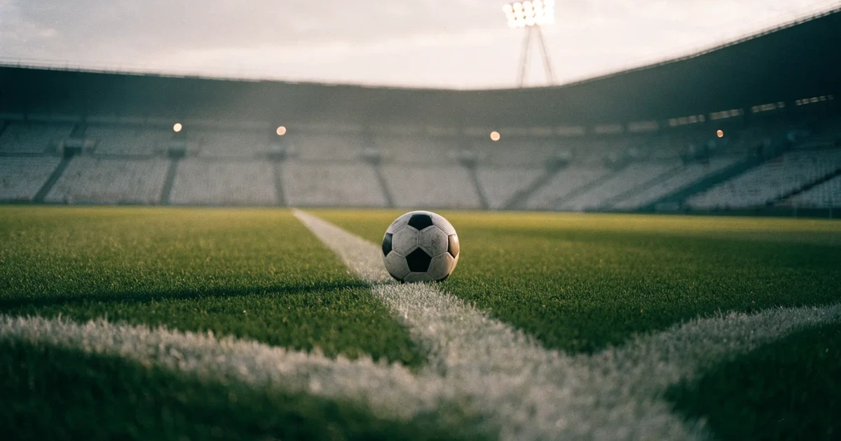 Ein Fussball liegt auf dem Anstosspunkt eines frisch gemähten Rasens, dahinter eine grosse Tribüne unter bewölktem Himmel