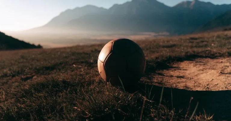 Ein Fussball auf einem staubigen Rasenstück in der Abendsonne, im Hintergrund eine hohe Bergkette