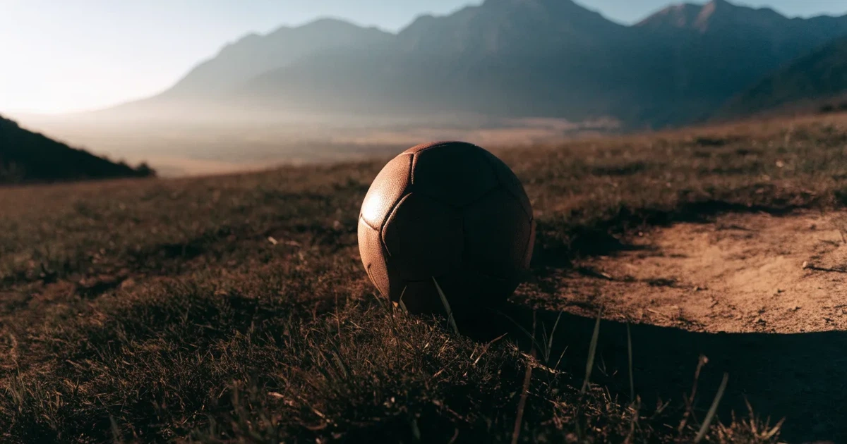 Ein Fussball auf einem staubigen Rasenstück in der Abendsonne, im Hintergrund eine hohe Bergkette